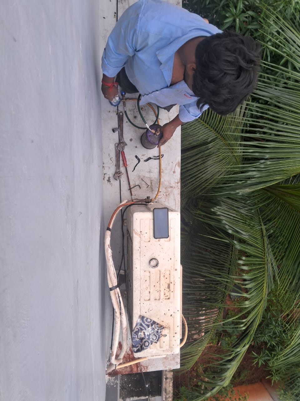 Technician servicing and repairing outdoor split air conditioner unit mounted on wall